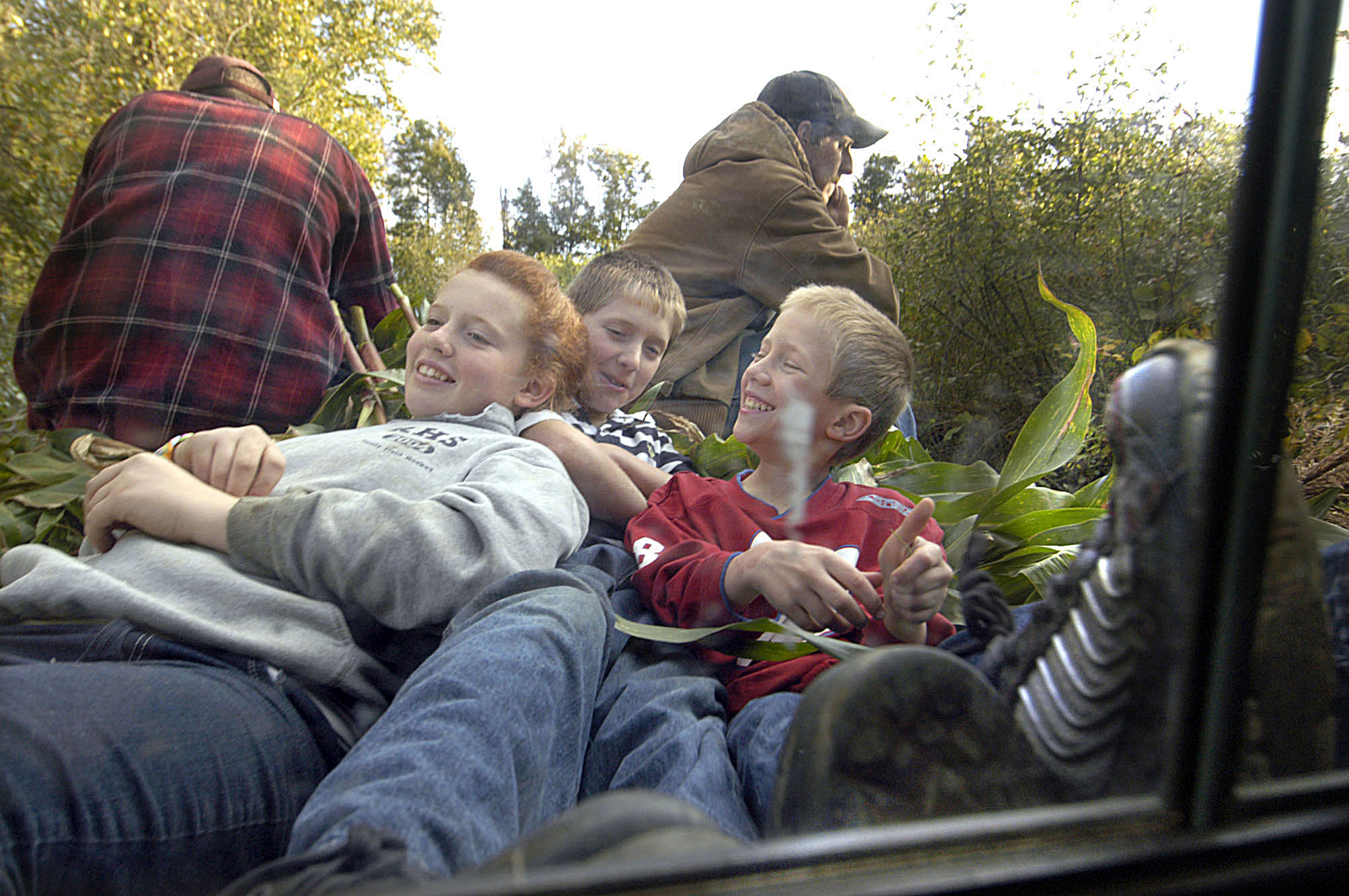 After a morning of picking corn on their family farm, kids ride the back of a pick-up truck filled with cornstalks they have just cut and bundled.