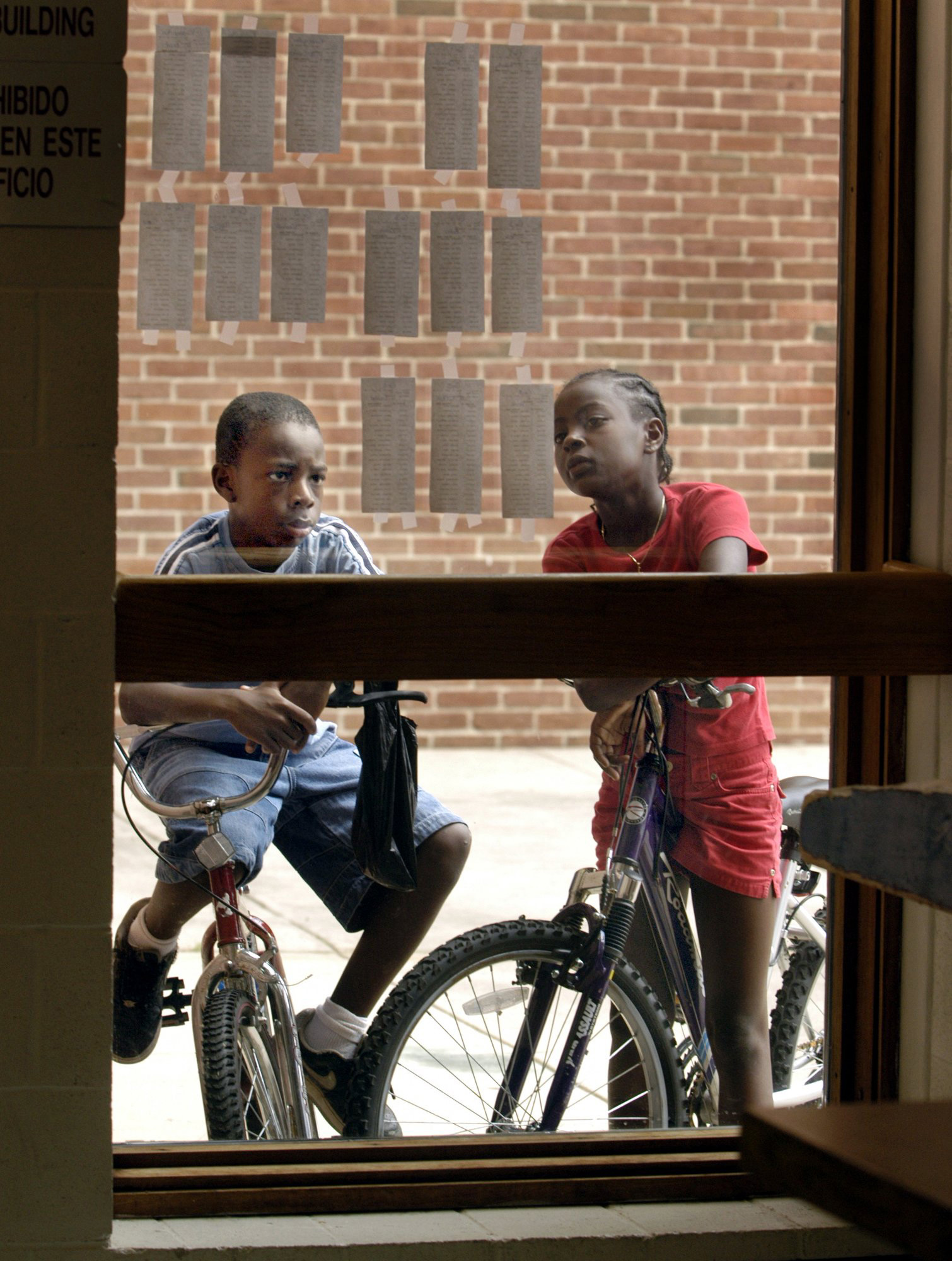 As Summer vacation comes to an end, two boys check out the posting of classes on the school window so they can know who this year's teacher will be. 